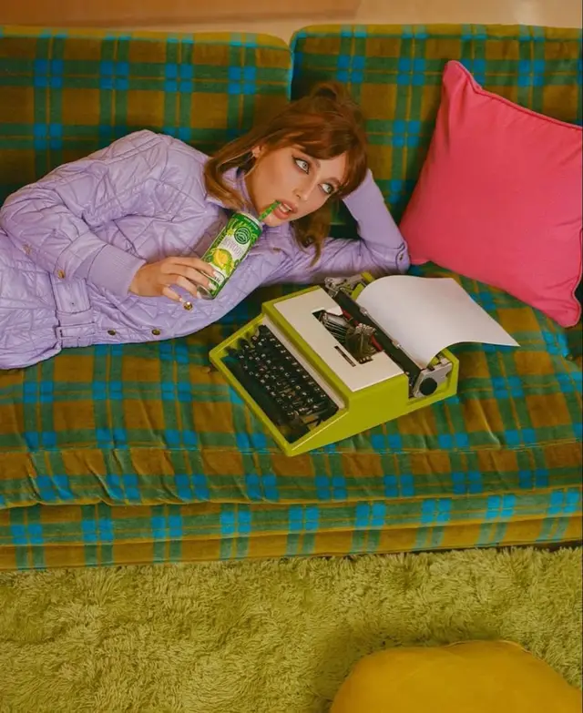 Retro living room: woman on green plaid sofa with lime-green typewriter and soda bottle