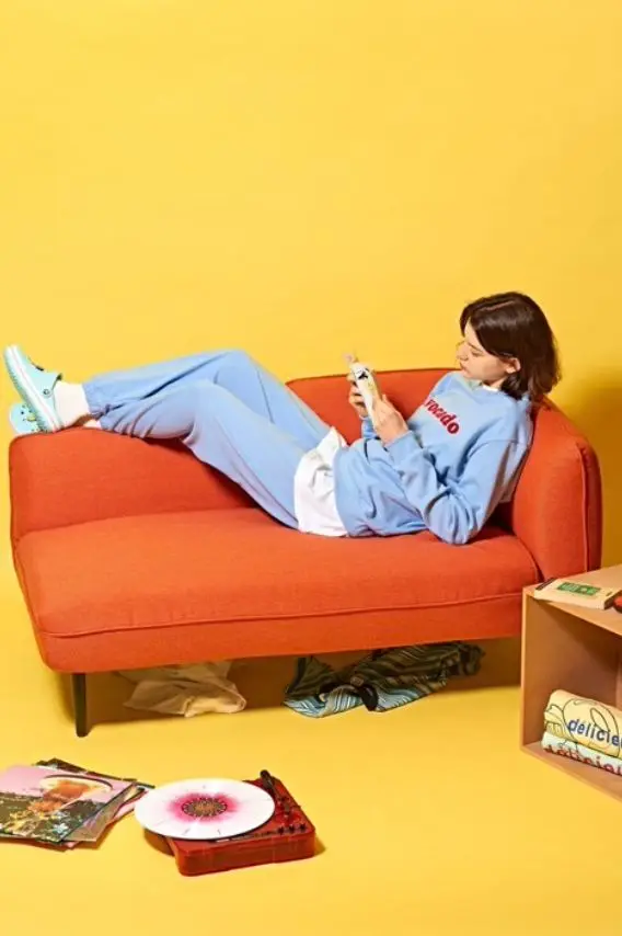 Casual lounge on orange loveseat with vinyl player and yellow backdrop