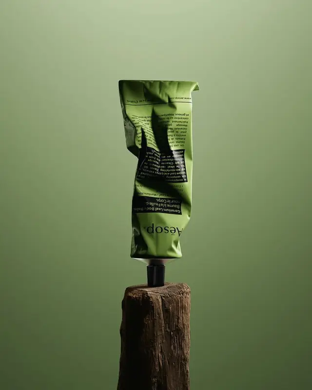 Aesop green hand cream tube balanced on weathered wood — minimalist product still life