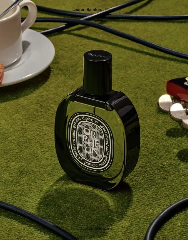 Diptyque Orphéon perfume bottle on moss-green felt with coffee and guitar cables