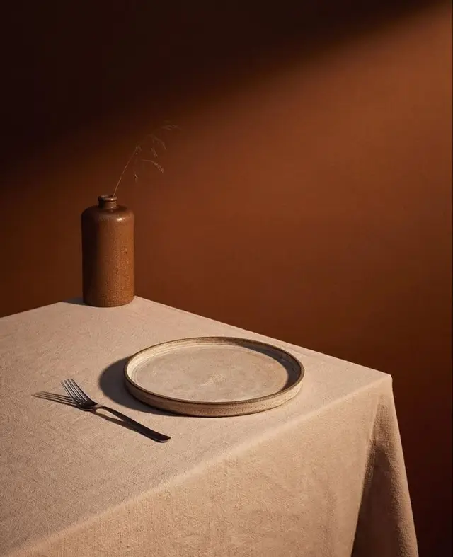 Minimal still life: linen tablecloth with stoneware plate and brown bottle vase
