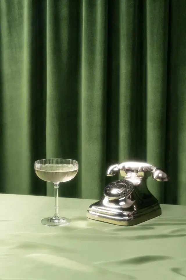 Chrome rotary phone and coupe glass on green velvet — still life photo