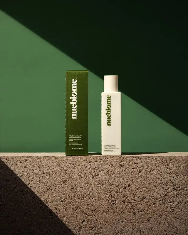muebiome Ferment Essence — white bottle with dark‑green box on textured concrete