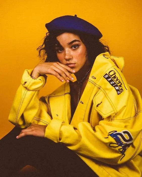 Studio portrait — oversized yellow "Cheerios Racing" jacket and navy beret