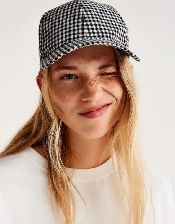 Winking portrait of young woman wearing black-and-white gingham baseball cap