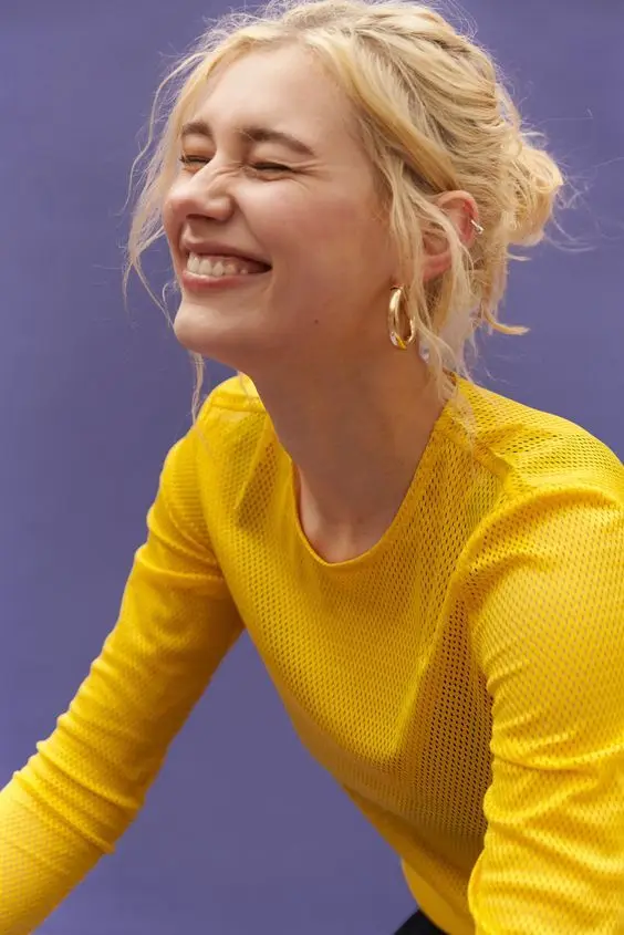 Studio portrait — woman in yellow mesh top laughing against purple backdrop