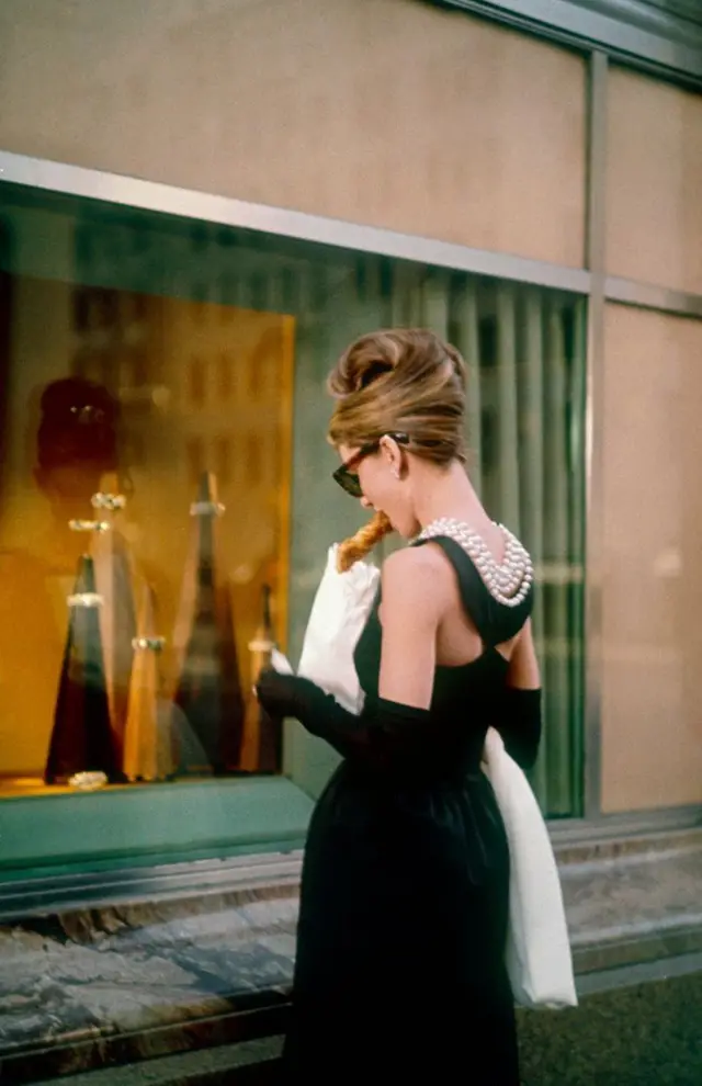 Woman in black cocktail dress with pearls window-shopping outside a jewelry store