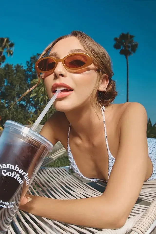 Close-up: woman in orange oval sunglasses sipping Chamberlain Coffee outdoors
