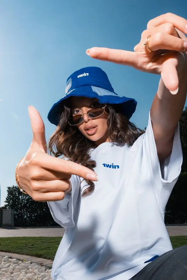 Low-angle streetwear portrait — blue bucket hat and "twin" logo tee
