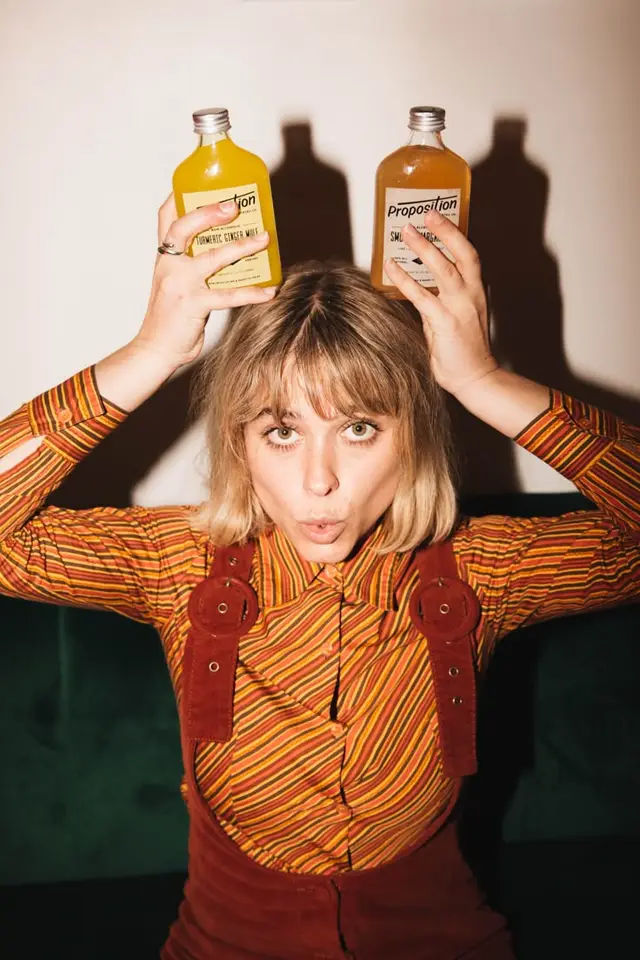 Playful portrait holding two 'Proposition' bottled drinks