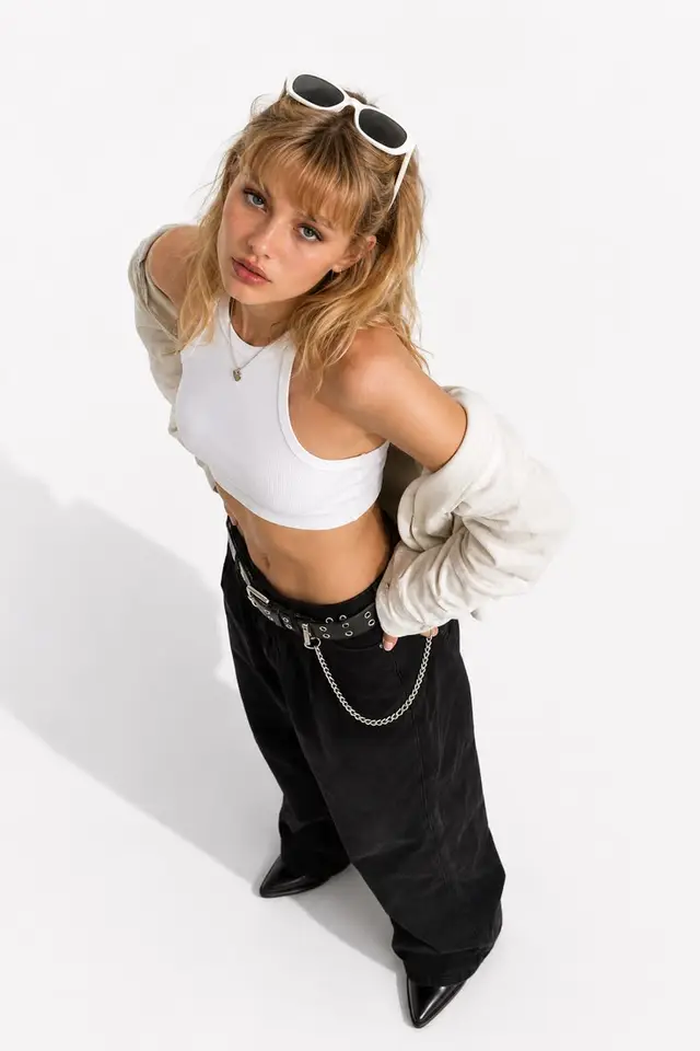 High-angle studio fashion shot — white ribbed crop top and baggy black pants with chain