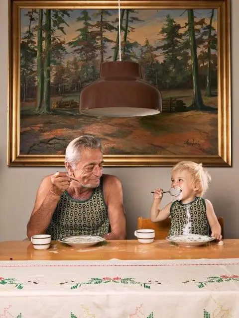 Older man and toddler in matching green patterned knit vests at wooden table
