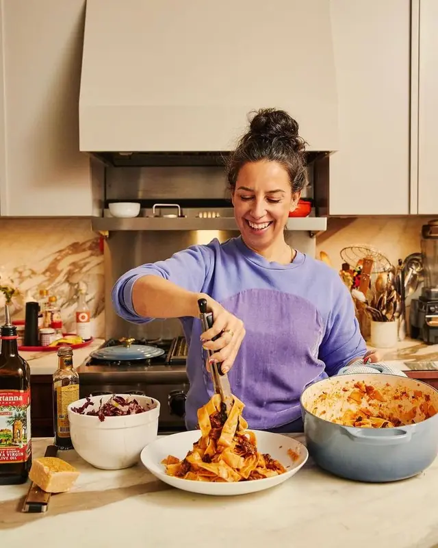 Woman Serving Pappardelle from Blue Dutch Oven in Marble Kitchen