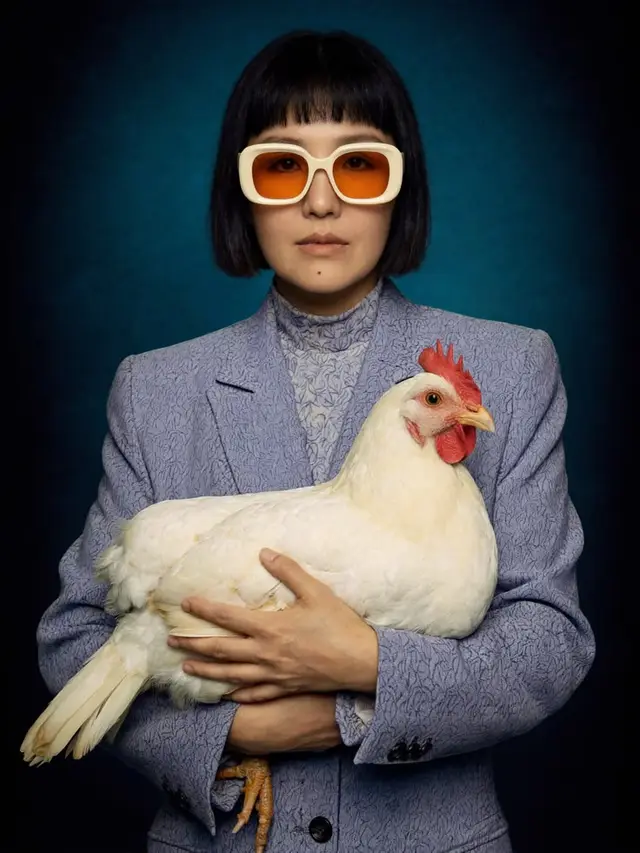 Studio portrait: person in lavender textured blazer holding a white hen