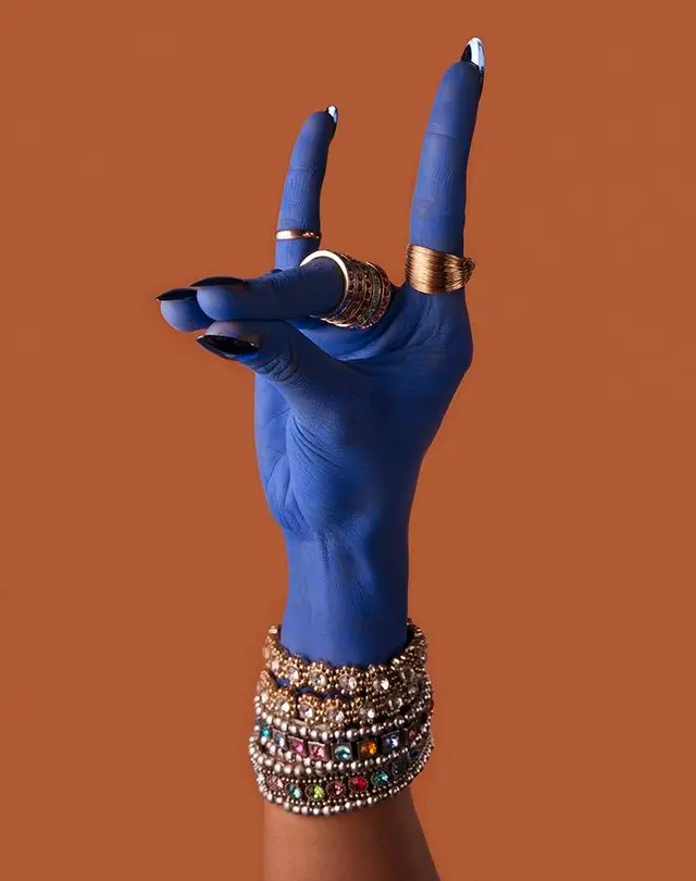 Cobalt-painted hand with gold rings and jeweled bangles on terracotta background