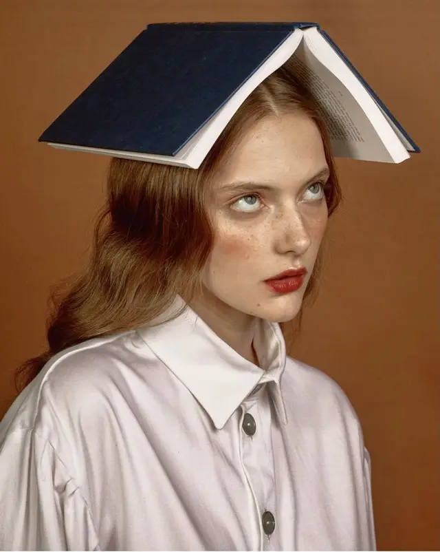 Editorial portrait — woman balancing open blue hardcover book on head