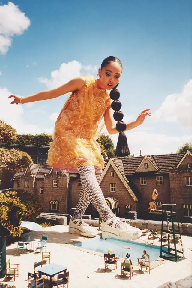 Surreal fashion editorial: model walking over dollhouse pool