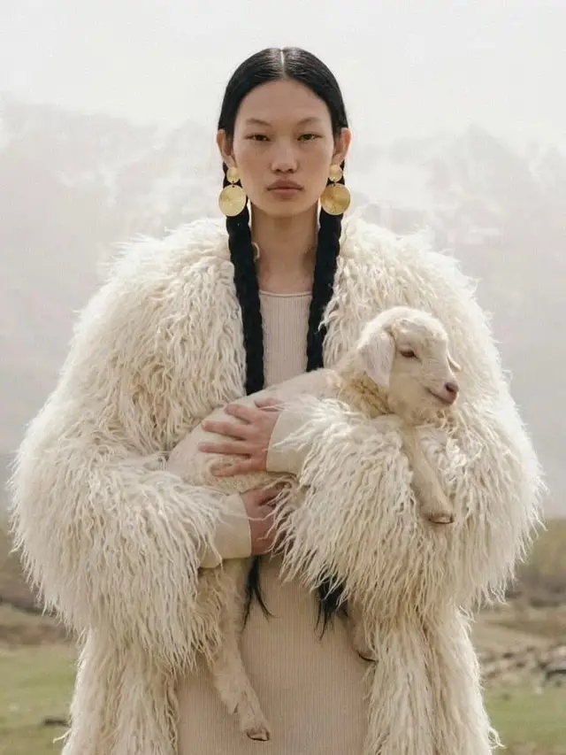 Model holding lamb in oversized white shearling coat with gold disc earrings