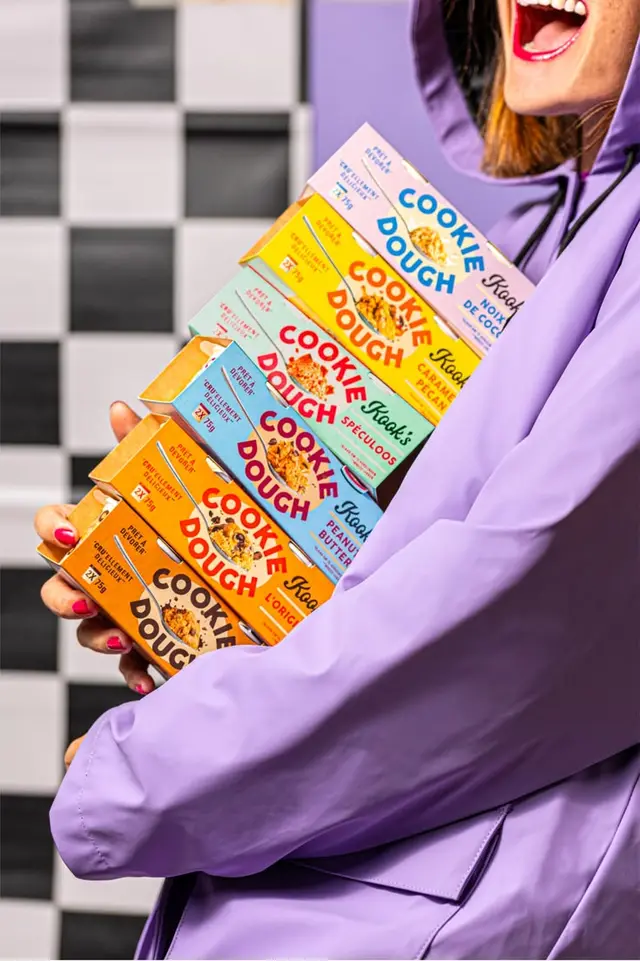 Stacked pastel "COOKIE DOUGH" snack boxes held by person in lavender jacket