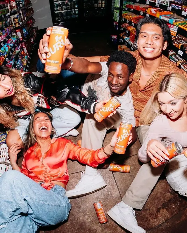 Friends in convenience store holding orange GURU energy drink cans