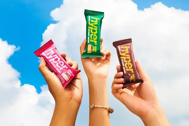 Three hands holding 'hyper' snack bars against blue sky