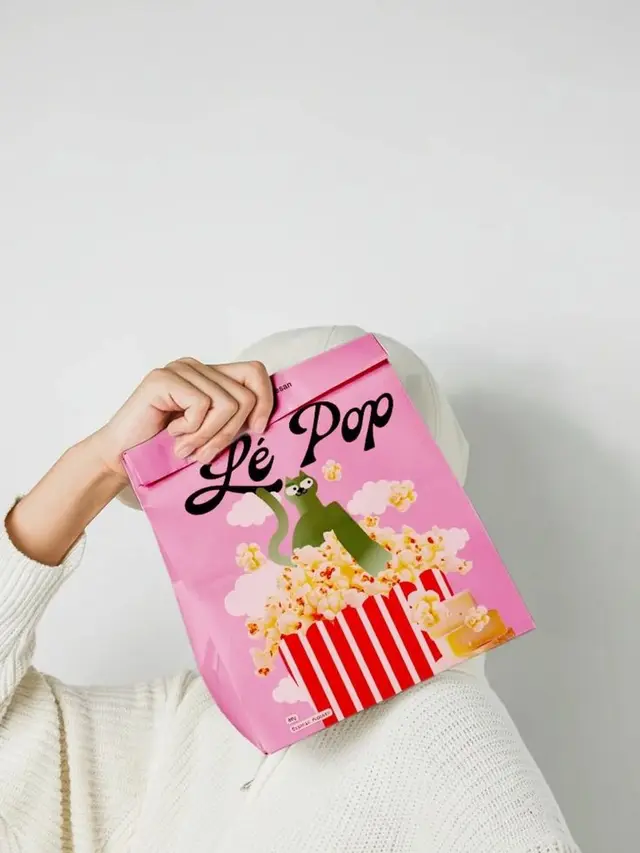 Pink "Lé Pop" popcorn bag with green cat illustration held by person in white sweater