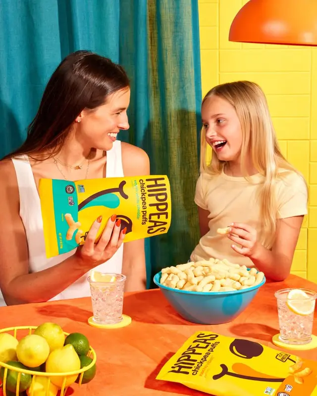 HIPPEAS chickpea puffs lifestyle photo — bright yellow packaging and blue snack bowl