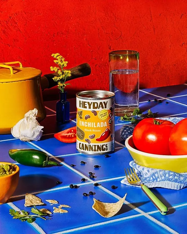 Heyday Enchilada black beans can on blue tile still-life with tomatoes and yellow pot