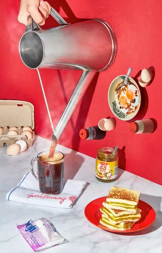 Surreal breakfast still life — watering can pours coffee over embroidered towel