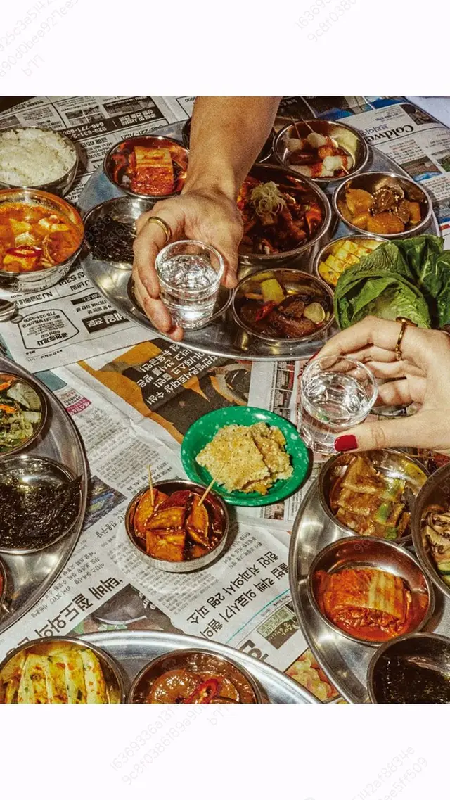 Korean banchan spread with soju on newspaper-covered table