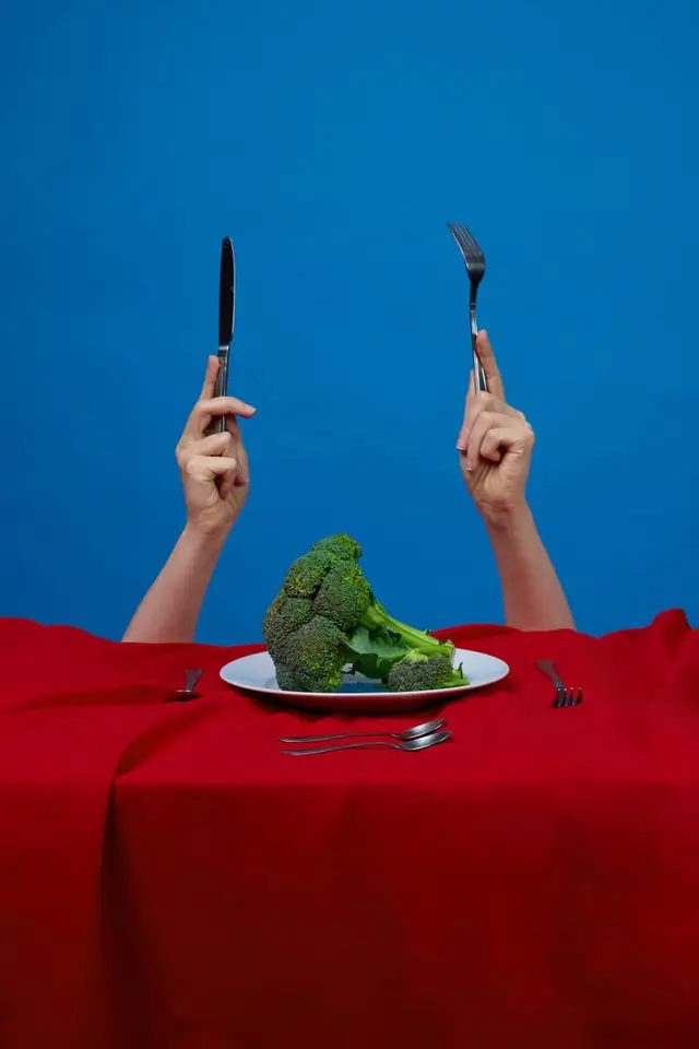 Surreal broccoli dinner — knife and fork raised over single broccoli on white plate