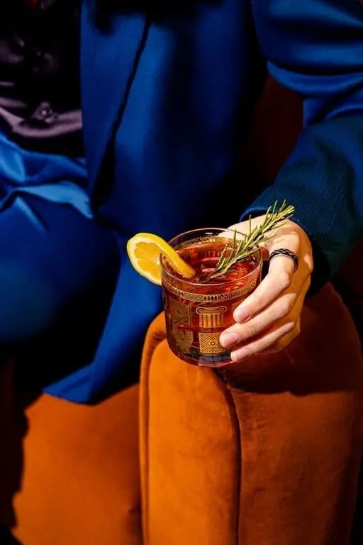 Patterned lowball cocktail with lemon wedge and rosemary on burnt-orange velvet