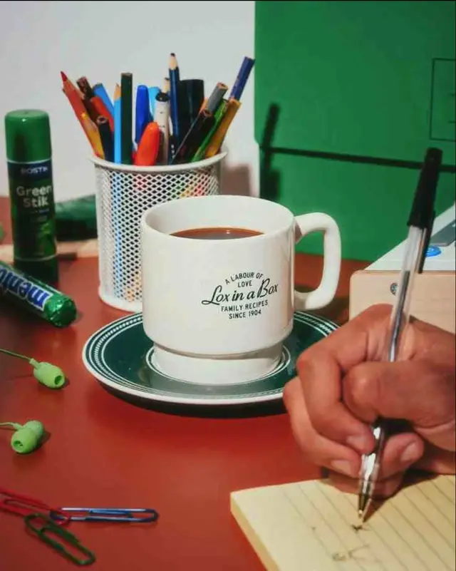 Coffee mug on saucer with pencils, Green Stik and Mentos on desk