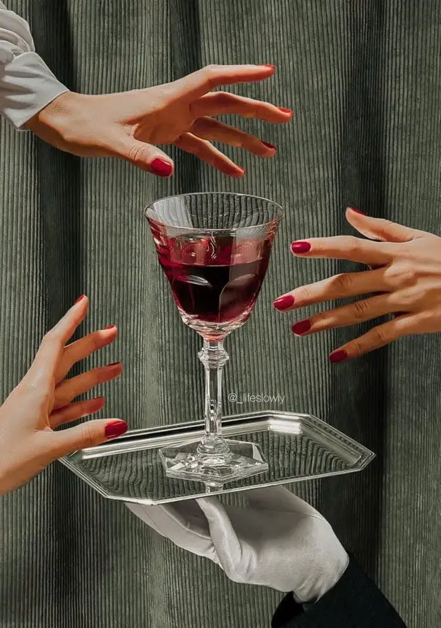 Cut-glass wine goblet on mirrored tray offered by gloved server, manicured hands reaching