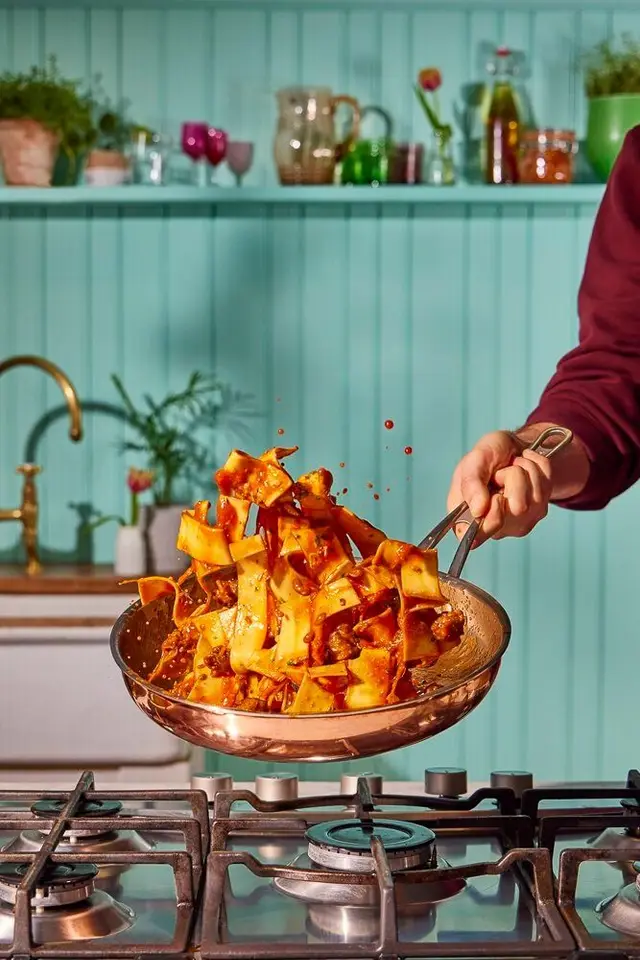 Pappardelle ragù tossed in copper skillet over gas stove in teal kitchen