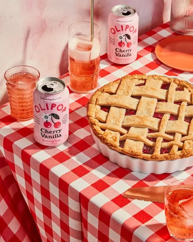 Olipop Cherry Vanilla cans with lattice cherry pie on red-and-white gingham