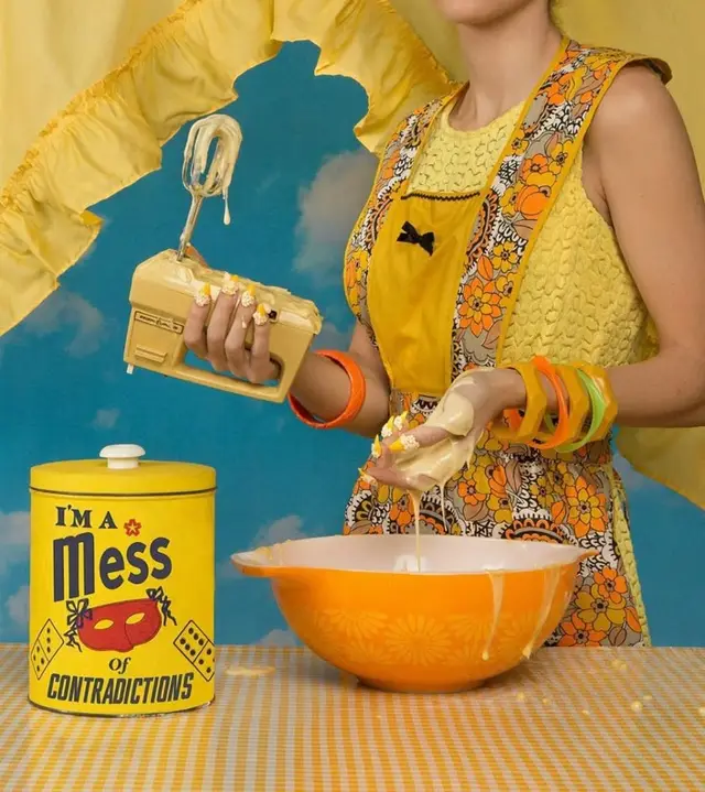 Retro 1970s kitchen tableau with yellow hand mixer and 'I'm a Mess of Contradictions' tin