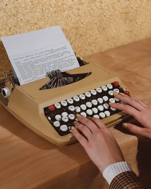 Beige portable typewriter on wooden desk with repeated "Please" typed