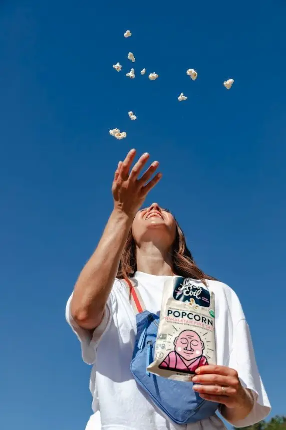 Low-angle shot of person tossing popcorn from branded bag against clear blue sky