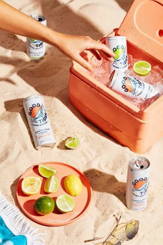 Good Tide hard seltzer cans in coral cooler on sandy beach with citrus