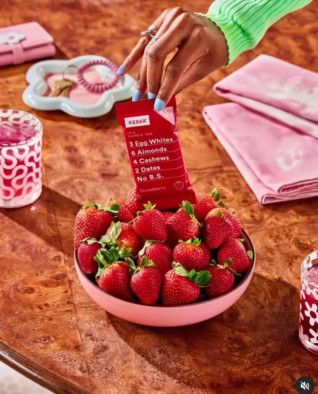 RXBAR Strawberry held over bowl of fresh strawberries on burl-wood table