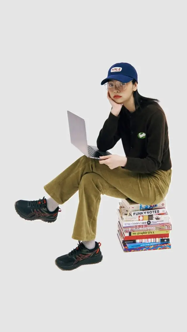Casual student portrait seated on stack of design books with laptop