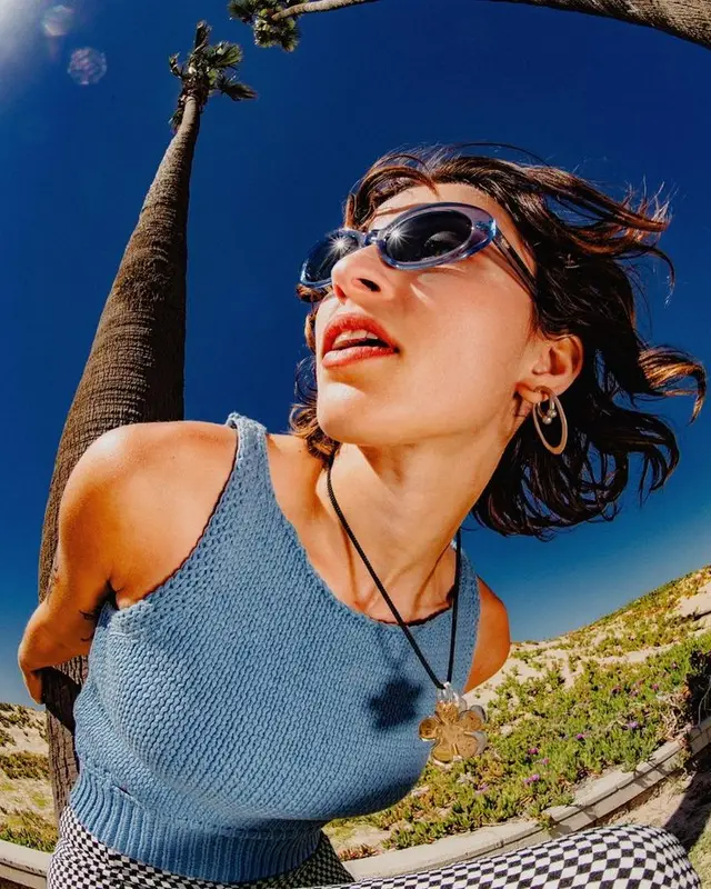 Low-angle fisheye portrait — blue knit tank and checkered pants by a palm tree