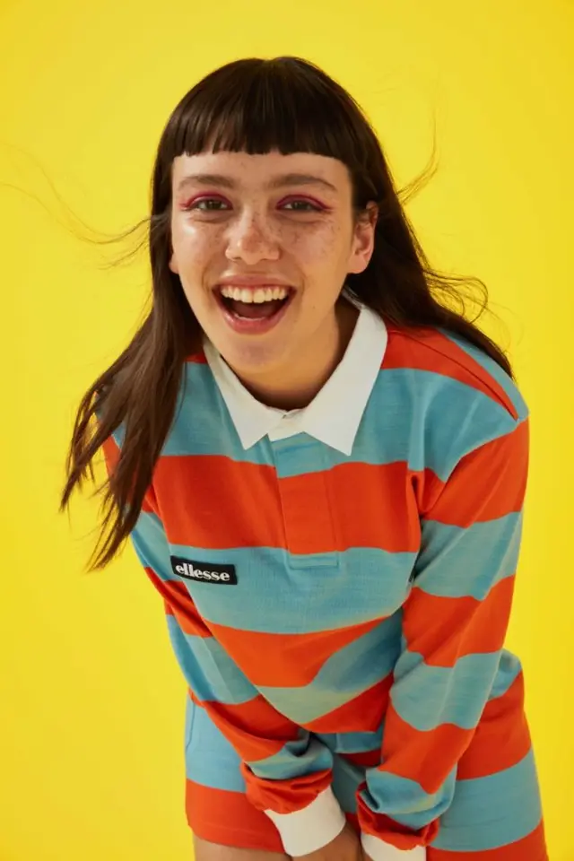 Smiling model in ellesse orange-and-blue rugby shirt on yellow backdrop