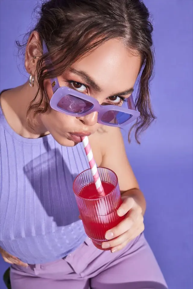Lavender fashion portrait — woman in purple sunglasses sipping pink drink