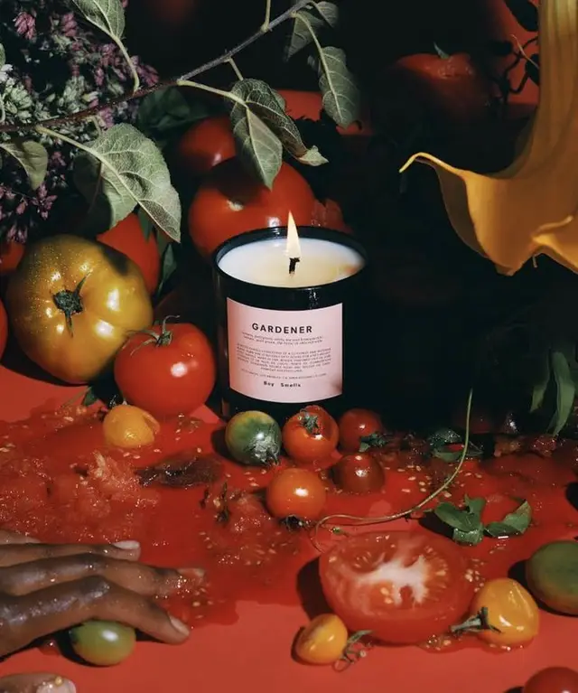 Lit 'GARDENER' candle amid smashed heirloom tomatoes — moody still life