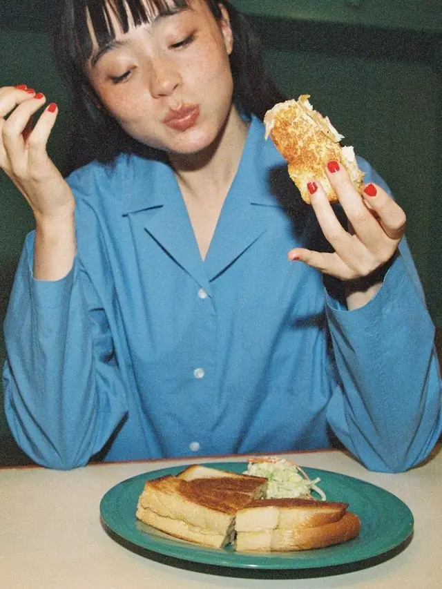 Candid film photo: person eating toasted sandwich on teal plate